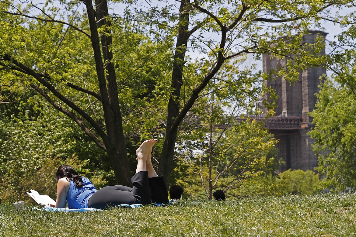 A woman reads a book while lying in the grass at Brooklyn Bridge Park during the current coronavirus outbreak, Sunday, May 17, 2020, in New York. (AP Photo/Kathy Willens)