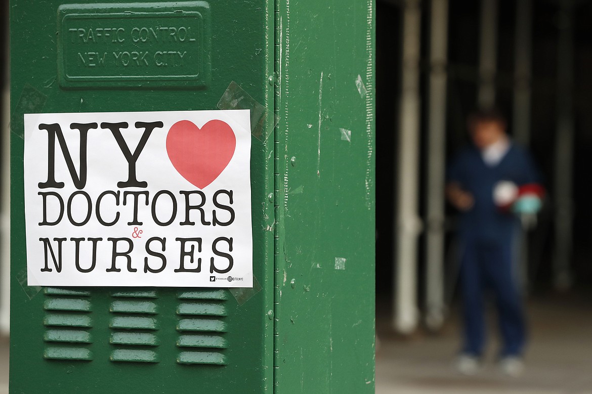 A sign acknowledging the work of doctors and nurses is posted on a traffic control box outside Brooklyn Hospital Center, as a hospital worker, right, waits for a traffic light to change before reporting to duty, Sunday, April 5, 2020, in New York. The Brooklyn hospital is one of several in the area treating high numbers of coronavirus patients. (AP Photo/Kathy Willens)