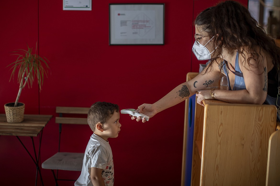 Hugo, 3, has his temperature taken by a teacher as he arrives at Cobi kindergarten in Barcelona, Spain, Friday, June 26, 2020. Spain's cabinet will extend the furlough schemes adopted during the coronavirus lockdown that brought the economy to a standstill until the end of September. (AP Photo/Emilio Morenatti)