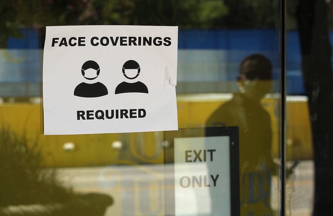 A man wearing mask to protect against the spread of COVID-19 is reflected next to a sign requiring face coverings at a business in San Antonio, Wednesday, June 24, 2020, in San Antonio. Cases of COVID-19 have spiked in Texas and the governor of Texas is encouraging people to wear masks in public and stay home if possible. (AP Photo/Eric Gay)