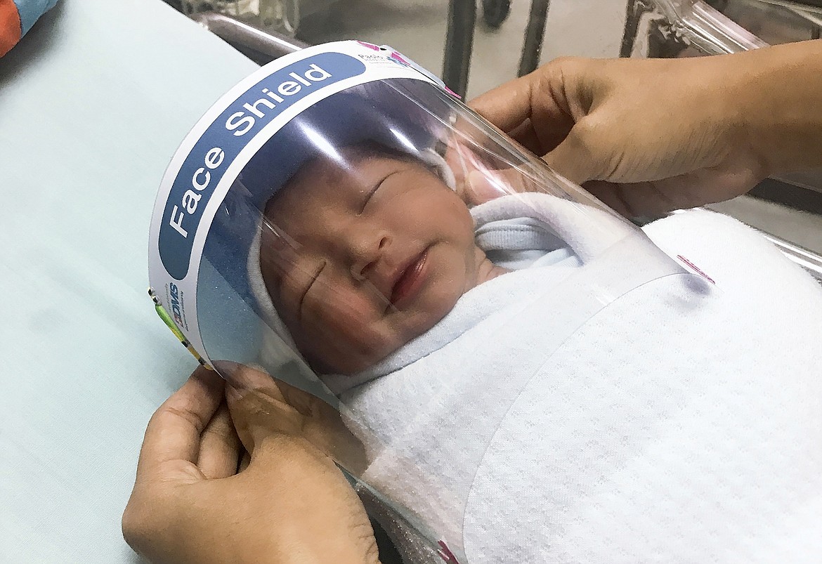 In this Friday, April 3, 2020, photo released by Paolo Hospital Samutprakarn, a nurse adjusts tiny face shield for a newborn baby to protect from new coronavirus at the newborn nursery of the hospital in Samutprakarn province, central Thailand. The new coronavirus causes mild or moderate symptoms for most people, but for some, especially older adults and people with existing health problems, it can cause more severe illness or death. (Paolo Hospital Samutprakarn via AP)