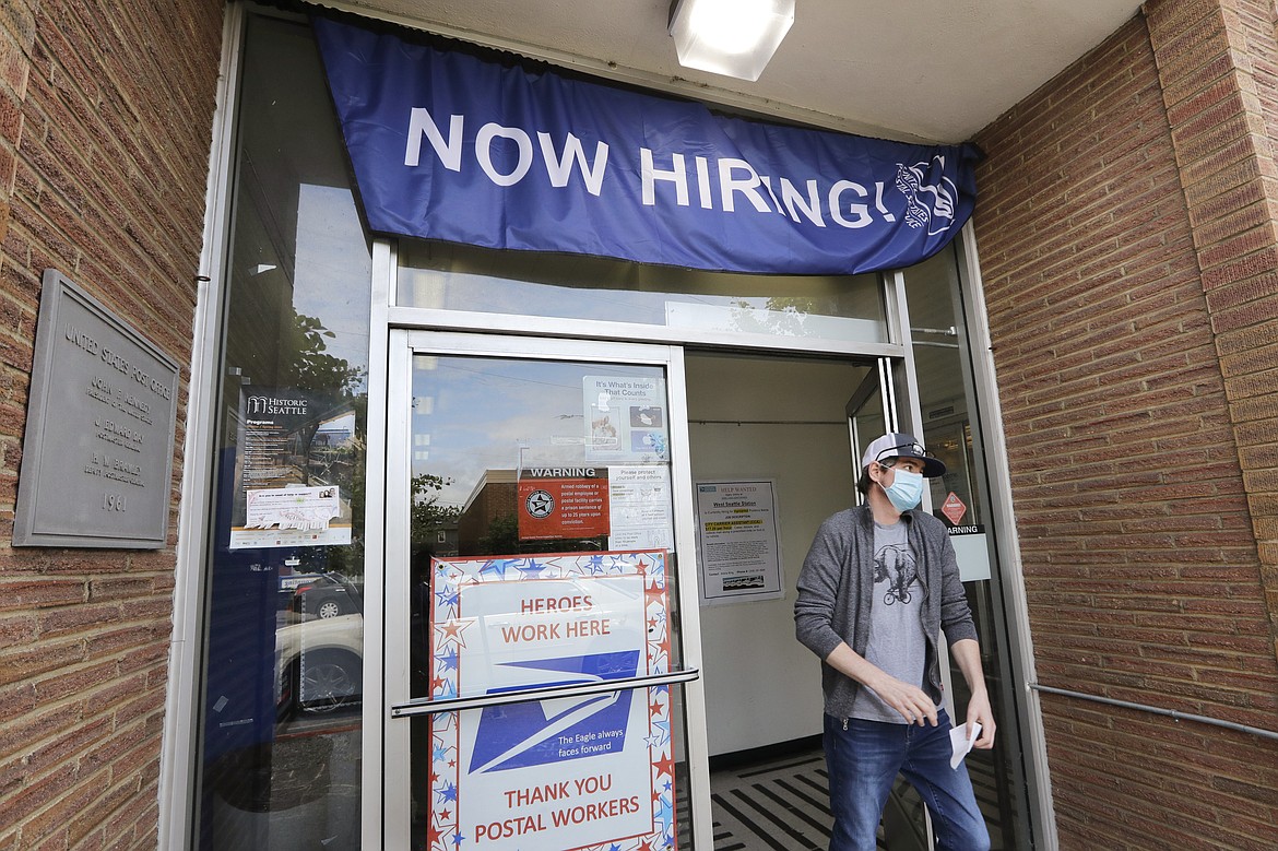 FILE - In this  June 4, 2020 photo, a customer walks out of a U.S. Post Office branch and under a banner advertising a job opening, in Seattle. The U.S. government is set to issue its latest report Thursday, June 11,  on the layoffs that have left millions unemployed but that have markedly slowed as many businesses have partially reopened and rehired some laid-off workers. (AP Photo/Elaine Thompson, File)