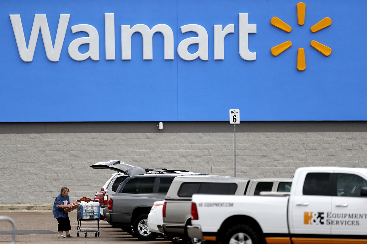 FILE - In this March 31, 2020 file photo, a woman pulls groceries from a cart to her vehicle outside of a Walmart store in Pearl, Miss. Walmart will require customers to wear face coverings at all of its namesake and Sam's Club stores. The company said the policy will go into effect on Monday, July 20, 2020 to allow time to inform stores and customers. (AP Photo/Julio Cortez, File)