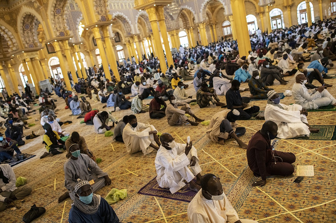 In this photo taken Friday, May 15, 2020, a follower of the Senegalese Mouride brotherhood, an order of Sufi Islam, films with his smartphone as he and others practice social distancing as they attend Muslim Friday prayers at West Africa's largest mosque the Massalikul Jinaan, in Dakar, Senegal. A growing number of mosques are reopening across West Africa even as confirmed coronavirus cases soar, as governments find it increasingly difficult to keep them closed during the holy month of Ramadan. (AP Photo/Sylvain Cherkaoui)