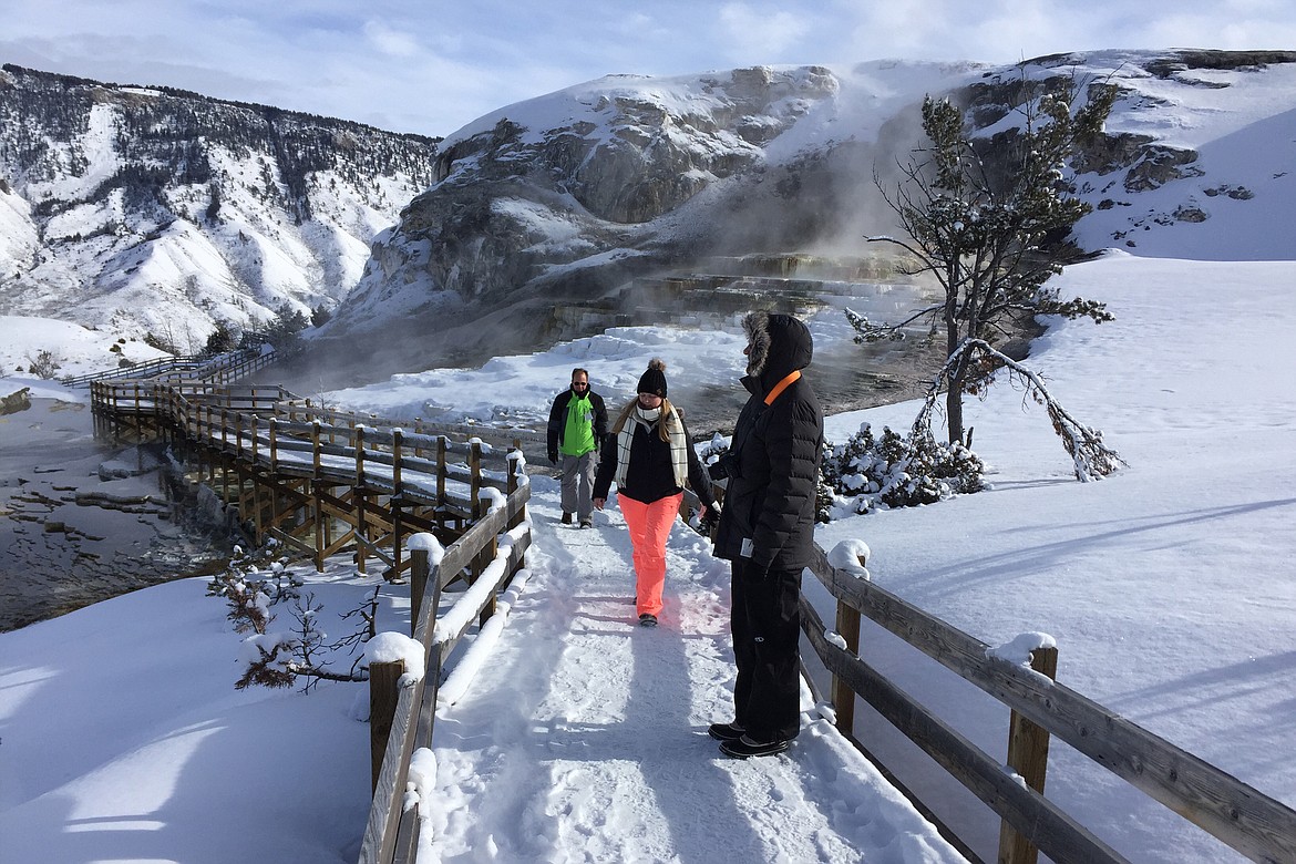 FILE - In this Jan. 20, 2017, file photo, James Kristy and Ginger Lee of Palm Beach County, Fla., walk the boardwalk at Mammoth Hot Springs in Yellowstone National Park, Montana. The superintendent of Yellowstone National Park says it likely won’t reopen until May 2020 or later, delaying the start of its traditional summer season for millions of tourists because of the coronavirus outbreak. Yellowstone and Grand Teton National Park have been closed since March 24, 2020, because of the virus. (AP Photo/Matthew Brown, File)