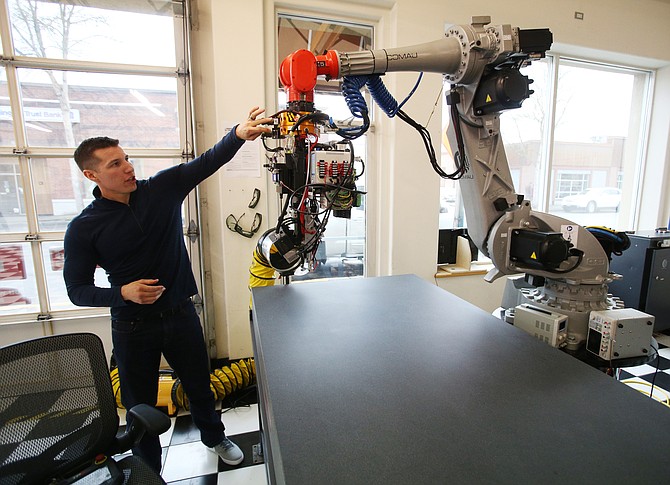 Continuous Composites Chief Executive Officer Tyler Alvarado shows one of the company’s robots that helps print composites using resins to make complex structures in free space.