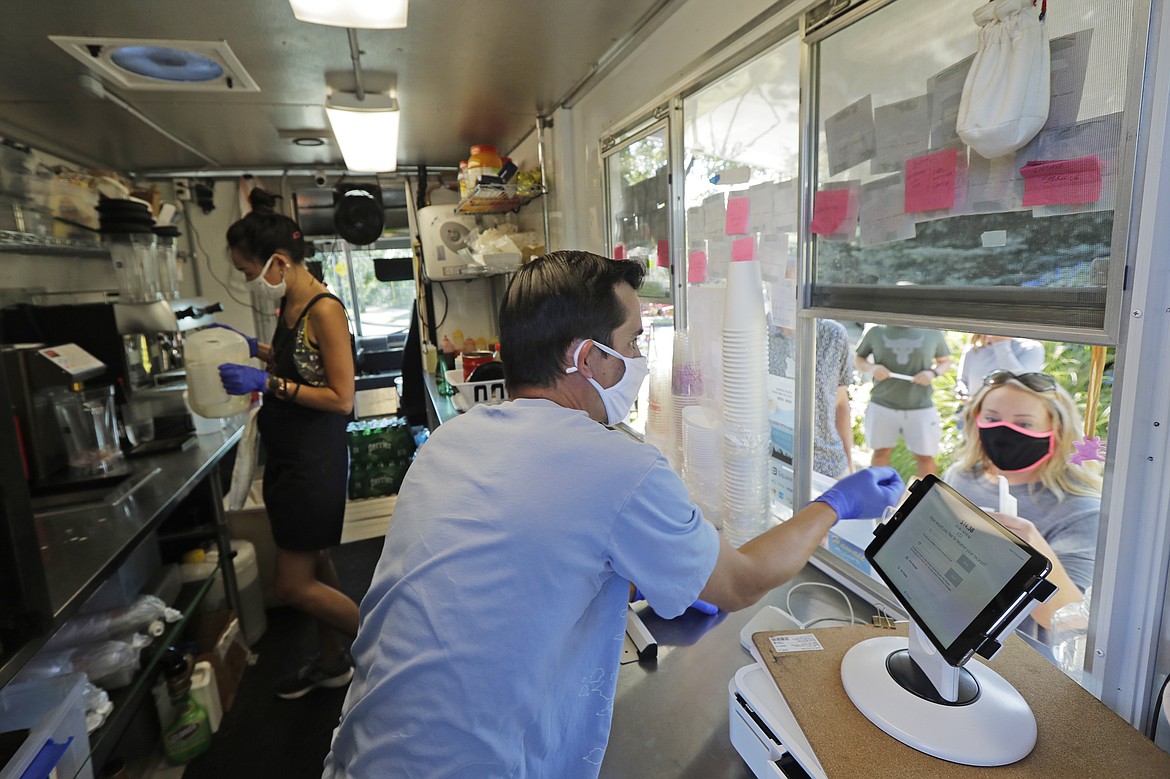 Athan Freitas, center, and Kaye Fan, left, make drinks and take orders in thier Dreamy Drinks food truck, Monday, Aug. 10, 2020, near the suburb of Lynnwood, Wash., north of Seattle. Long seen as a feature of city living, food trucks are now finding customers in the suburbs during the coronavirus pandemic as people are working and spending most of their time at home. (AP Photo/Ted S. Warren)