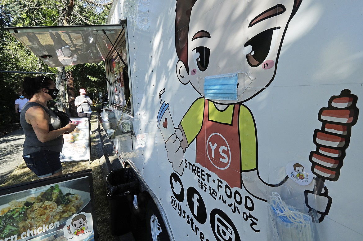 A customer orders from the YS Street Food food truck, Monday, Aug. 10, 2020, near the suburb of Lynnwood, Wash., north of Seattle. Long seen as a feature of city living, food trucks are now finding customers in the suburbs during the coronavirus pandemic as people are working and spending most of their time at home. (AP Photo/Ted S. Warren)