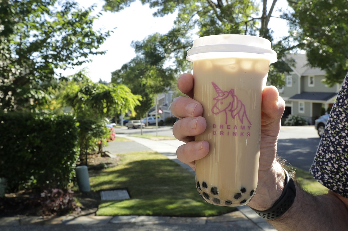 Greg Schwab holds a boba tea he ordered from the Dreamy Drinks food truck, Monday, Aug. 10, 2020, near the suburb of Lynnwood, Wash., north of Seattle. In June, Greg's wife Julie Schwab started organizing a regular schedule to bring food trucks to their neighborhood as a way to both help small businesses and give families staying at home during the coronavirus pandemic different options for meals. Long seen as a feature of city living, food trucks are now finding customers in the suburbs during the coronavirus pandemic as people are working and spending most of their time at home. (AP Photo/Ted S. Warren)