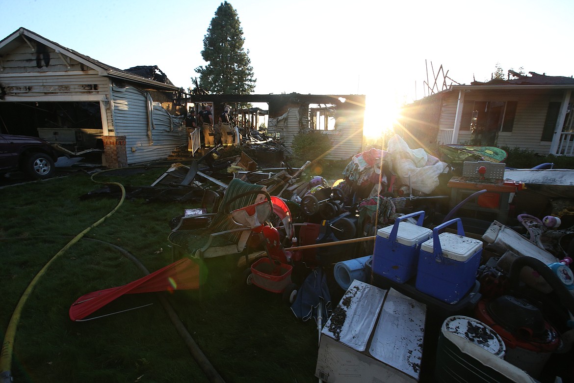 A setting sun casts a glow over two Post Falls homes destroyed in a fire Friday night, as firefighters look over the scene.