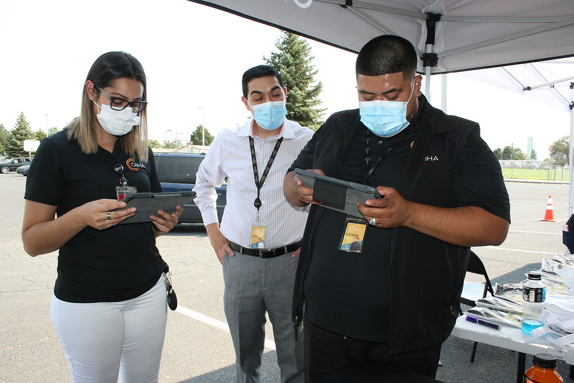 Rosa Martin, left, and Eduardo Saldivar, right, were volunteering at the drive-through census event in Mattawa when they realized they hadn't filled out census forms. Carlos Ruiz of the Mattawa CBHA clinic watches their progress.