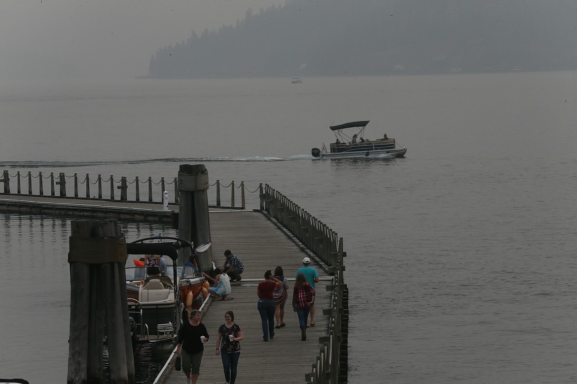 People walk on The Coeur d'Alene Resort Boardwalk as a boat heads out onto the smoky waters of Lake Coeur d'Alene on Thursday. Rain is expected this weekend after one of the driest summers in history.