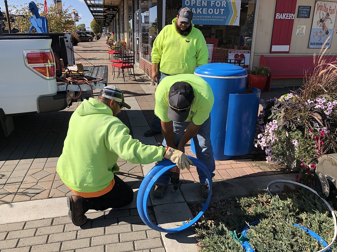 Moses Lake City maintenance worker Reuben Valdez, with the help of Berto Chavez (kneeling) and Manny De La Torre (standing) drills a hole in the sidewalk in front of the Red Door Cafe Thursday morning to secure one of the new trash receptacles.