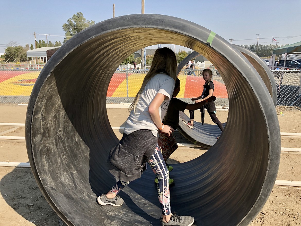 Ten-year-old Parker Gordon (front) and her siblings Decker, 5, and Charlie, 7, roll a section of pipe along a track at the opening day of Country Cousins' Harvest Festival in Othello on Saturday.