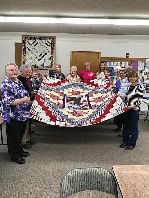 Quilters of St. George’s parish pose with a special quilt made for a vet. The group made and donated some 200 quilts last year to 17 locations last year.