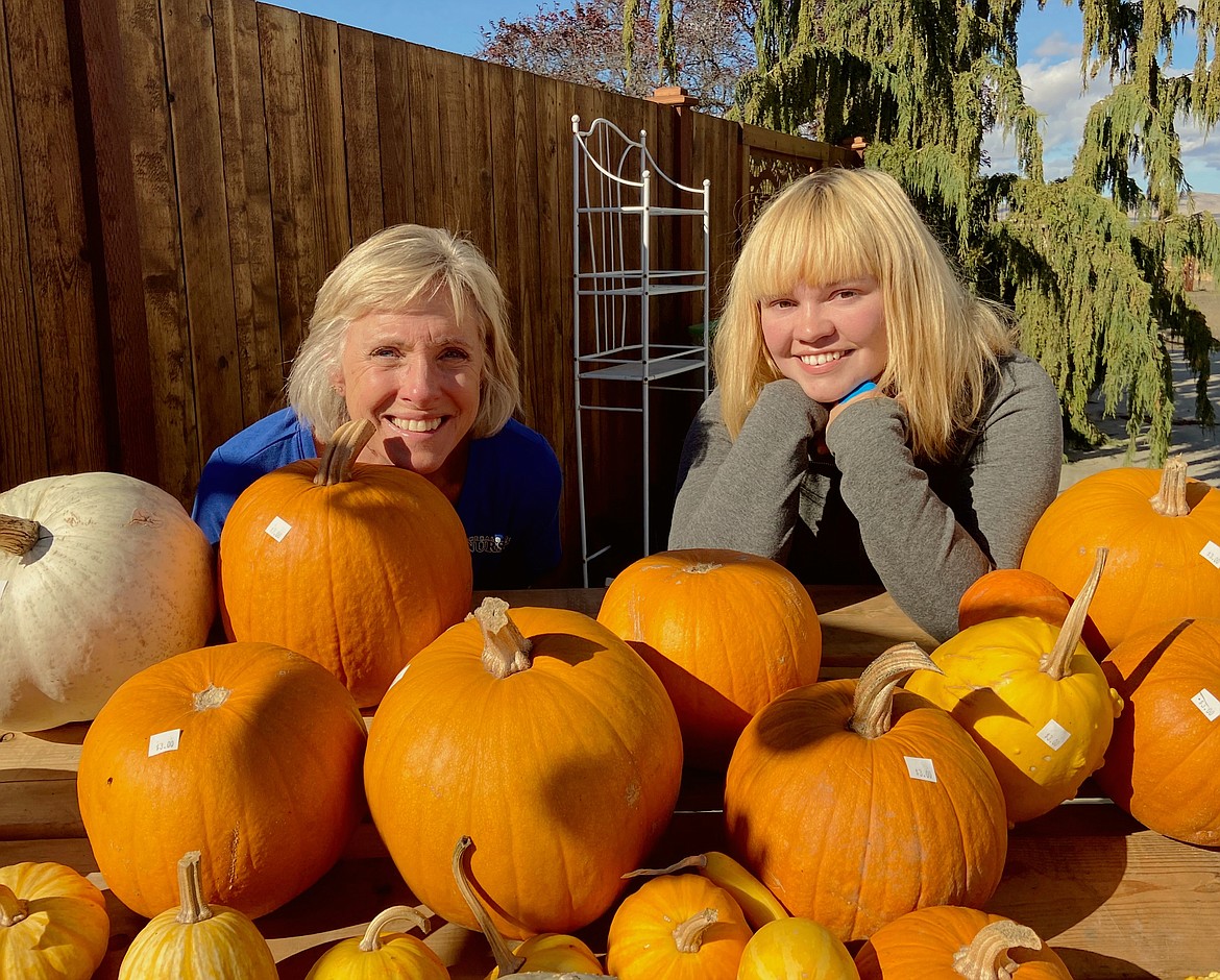 Nancy Richardson (left) and Katherine Moore peer out from behind a pile of pumpkins for sale at Emerald Desert Nursery.