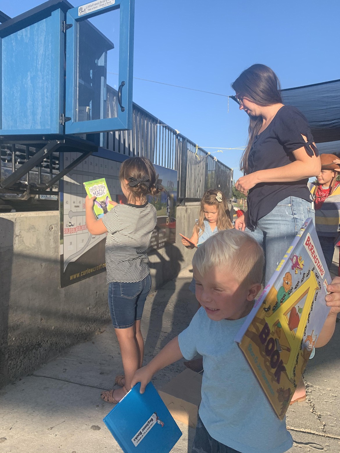 Louis Larsen, front, walks away from the Little Free Library with a smile and books in hand, while Tia Allred and her two daughters pick out books behind him.