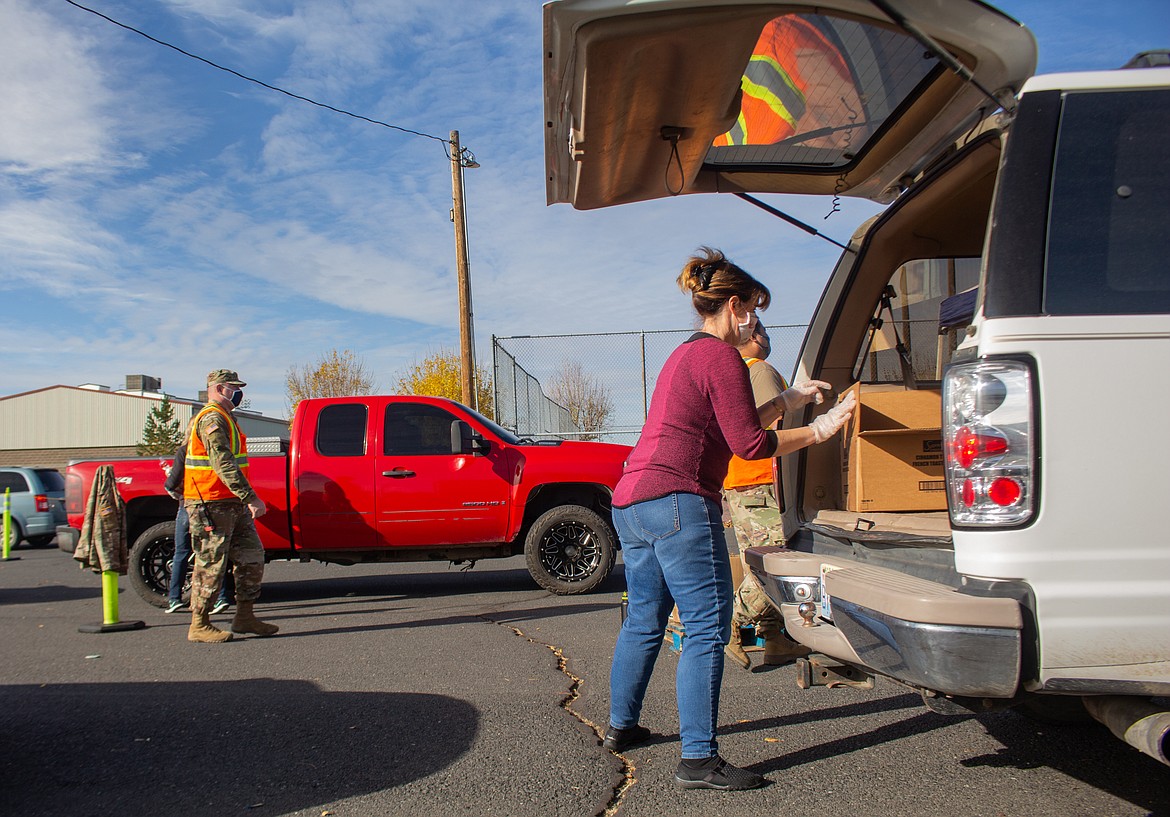 Cheryl McCort, front right, loads up food items into the back of car while Washington Army National Guard members help coordinate traffic in the background at the Second Harvest Mobile Market event in Othello on Tuesday.