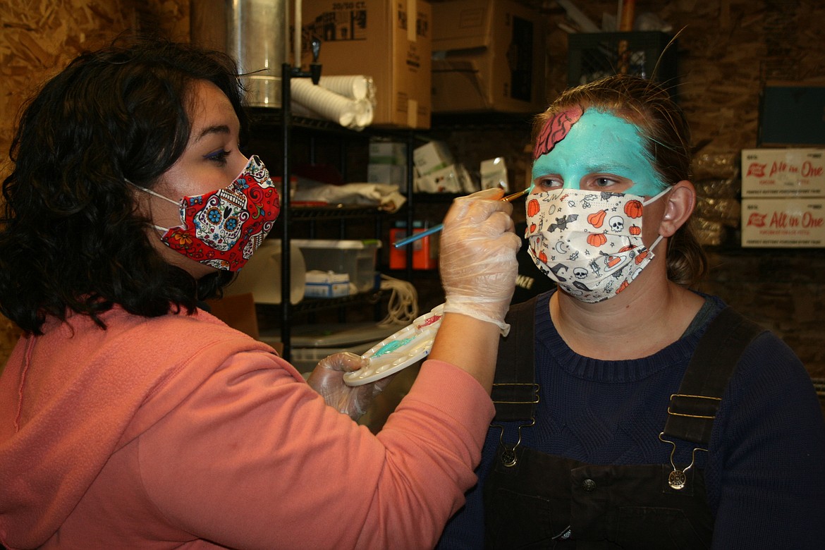 With the help of face paint, Stephanie Carl (left) transforms Paula Robertson (right) into a zombie with her brains falling out for the Othello Rodeo Association straw maze.