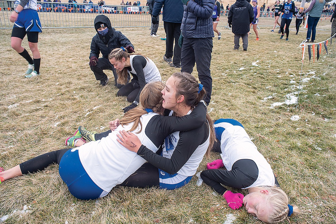 The Columbia Falls girls cross country team recovers after the state A finals in Kalispell. Hannah Sempf hugs teammate Alyssa Blankenship, Siri Erickson hugs the ground and assistant coach Shelby Johnson checks on Emma Upton, who is throwing up. (Chris Peterson photo)