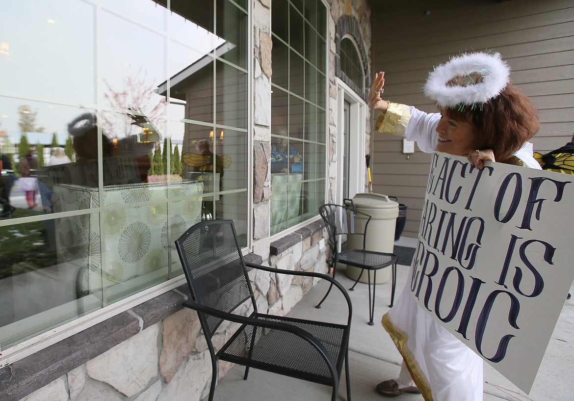 Silver Angels for the Elderly volunteer Peggy Lemm waves through the window to Renaissance at Coeur d'Alene residents during a Halloween parade Friday. Her sign reads, "The act of caring is heroic."