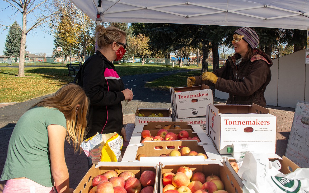 Kristi Juette and her daughter, Marissa, pick up some apples from Rachel Naff at the Tonnemaker Hill Farms booth on Saturday at the Moses Lake Farmers Market.