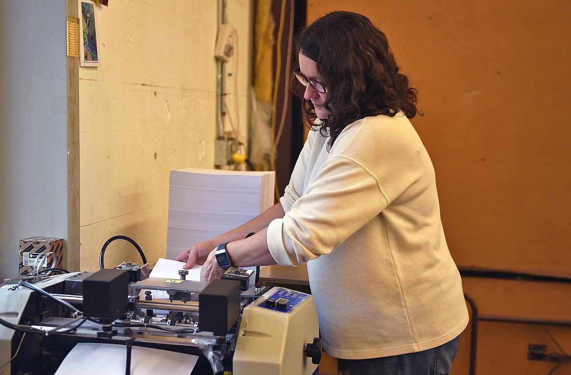 Top Copy's graphic designer Cindy Gillund feeds blank paper into the perforator machine at the print shop. (Whitney England/Whitefish Pilot)