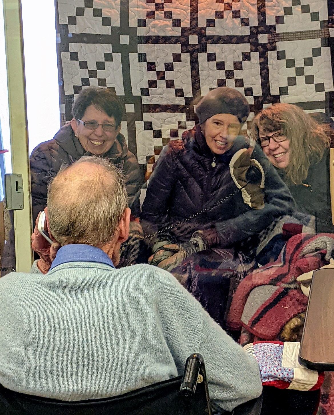 World War II veteran and Montana Veterans Home resident Jack Dunn visits through the glass door with his daughters, Kathy Dunn Hoff, Dianne Guenther and Cindy Babon Tuesday. (photo provided)