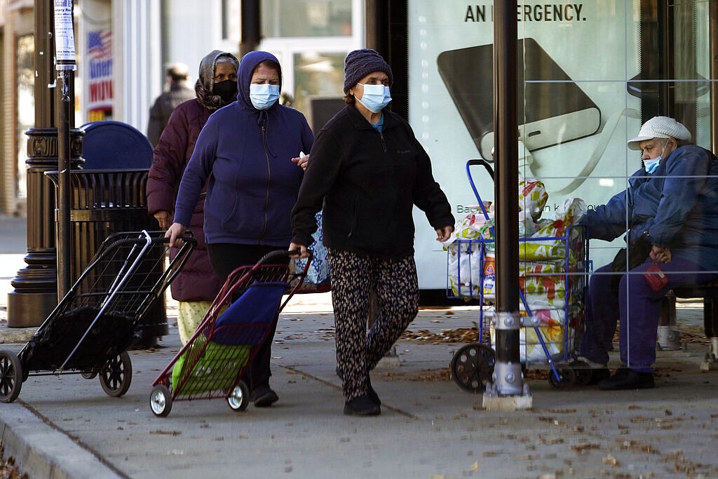 In this Nov. 12, 2020, file photo, people wear a face masks as they walk to an ICNA (Islamic Circle of North America) Relief Resource Center and Food Pantry during the COVID-19 pandemic in Chicago. In states like New Mexico and Washington and cities such as Philadelphia to Chicago, leaders are ordering or imploring residents to stay home to help stem a rising tide of infections that threatens to overwhelm the health care system.