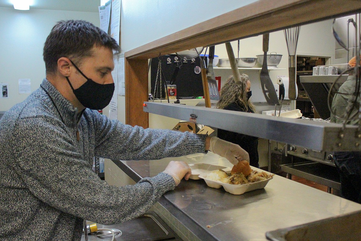 Volunteer John Killian takes trays of food ready to be handed out as they are prepared in the kitchen at the Elks Lodge in Moses Lake on Wednesday afternoon.