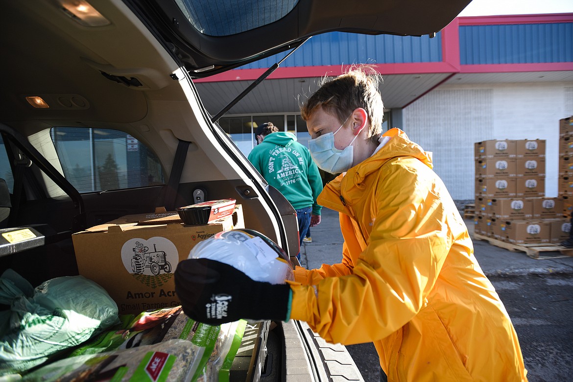 Volunteer Aiden Skees, an 8th-grader at Cayuse Prairie School, places a frozen turkey in the back of a vehicle during the Flathead Food Bank's Thanksgiving meal distribution on Friday. Skees was one of several students and staff volunteering from Cayuse Prairie. (Casey Kreider/Daily Inter Lake)