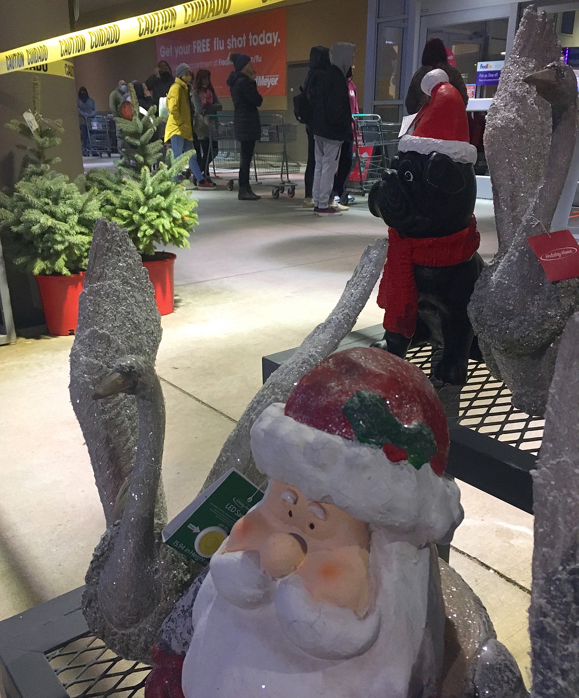 Santa statues stand outside Fred Meyer as shoppers wait to enter the store Friday morning