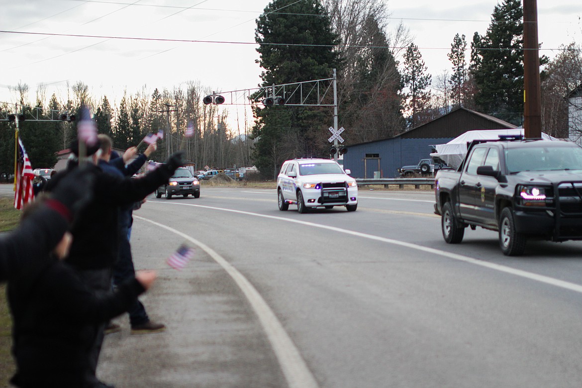 A crowd of supporters waves American flags as a procession of police and other first responders passes by on Highway 200 next to Elks Golf Course.