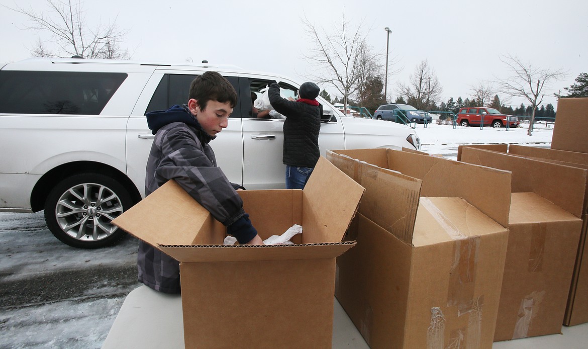 Cason Sperber, 13, grabs meal-filled bags out of boxes on Monday as he helps give out thousands of meals to local families at Lake City High School. Meals were also given away curbside at Coeur d'Alene High.
