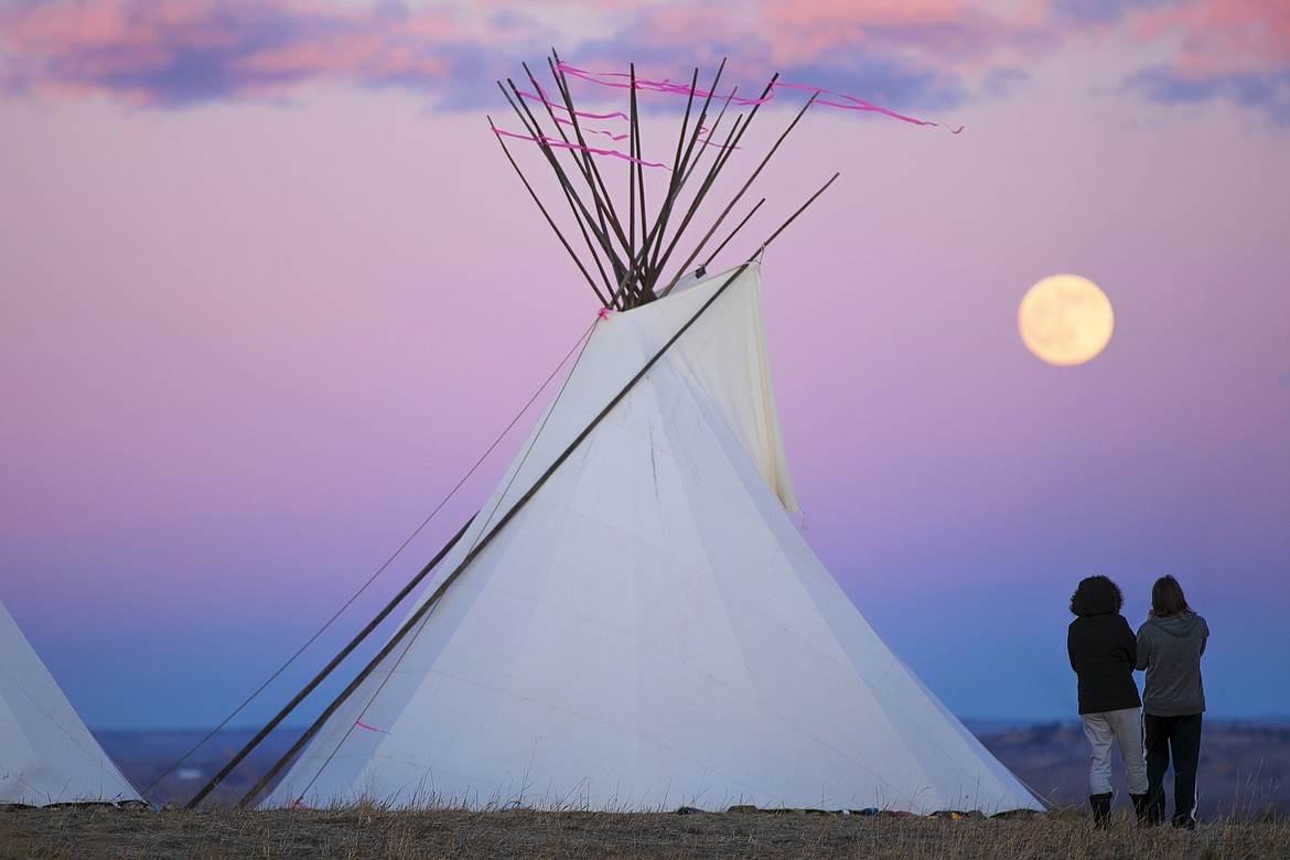 A couple watches the Cold Moon while standing amongst "The Lighting of the Teepees: A Symbol of Hope" at Swords Park Tuesday, Dec. 29, 2020 in Billings, Mont. (Ryan Berry/The Billings Gazette via AP)