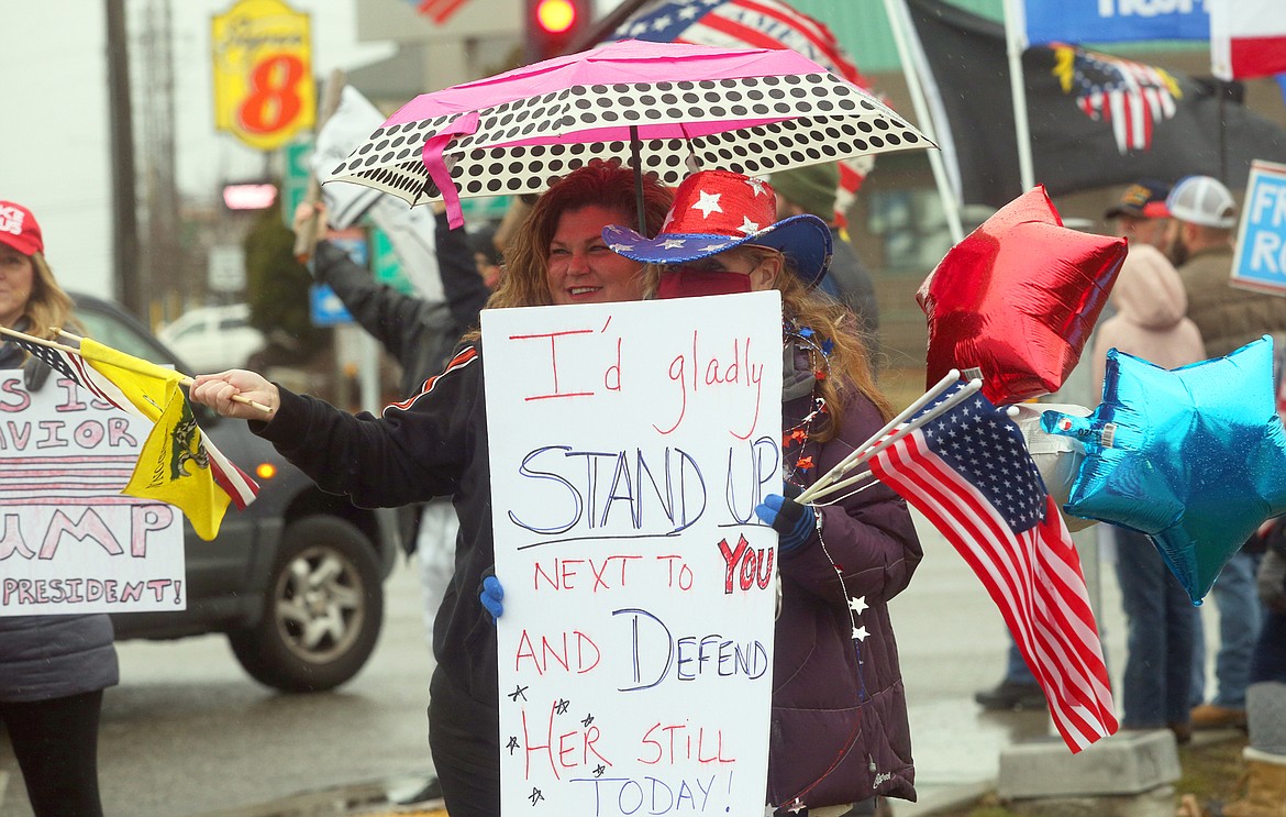 Lori Green, left, and Patty Stanfield, hold flags and balloons as they huddle under an umbrella and wave to passersby during Wednesday' pro-Trump rally in Coeur d'Alene.