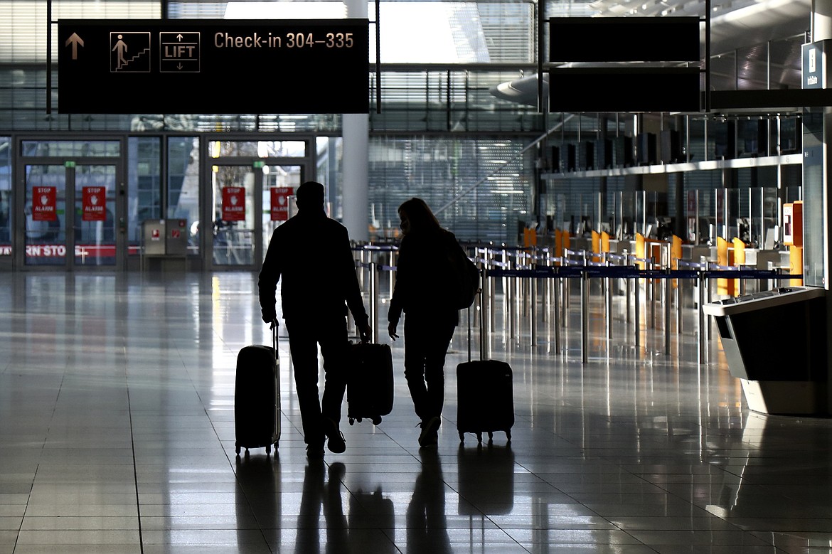 In this Saturday, Dec. 26, 2020 file photo, people walk with their luggage through a deserted check-in hall at the airport in Munich, Germany as Germany continues its second lockdown to avoid the further outspread of the coronavirus. On Tuesday, Jan. 12, 2021, the U.S. government said it will require airline passengers entering the country to show proof of a negative COVID-19 test before boarding their flights. It will take effect Jan. 26.