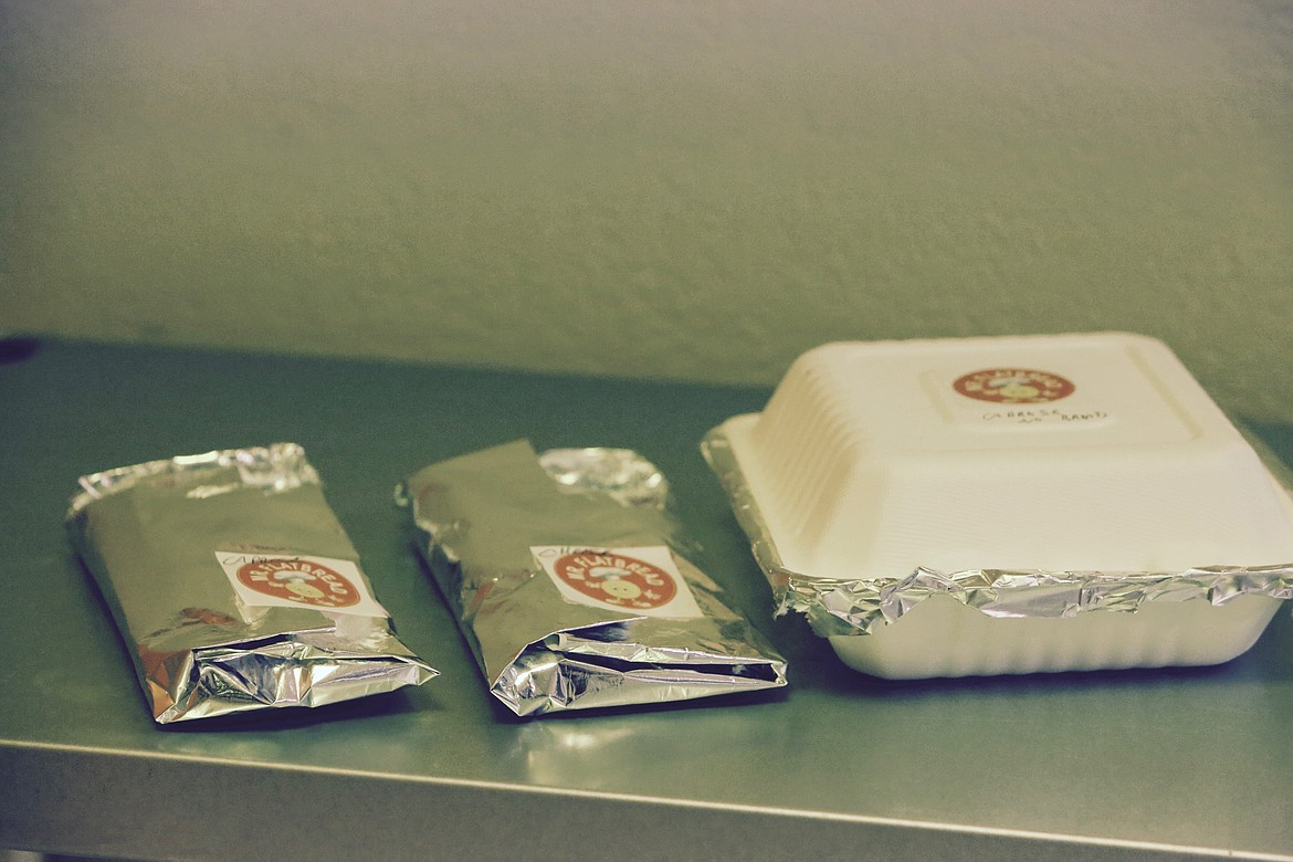 A pair of flatbreads and a salad, both well sealed with aluminum foil to keep the food warm, sit ready to be picked up by a customer.