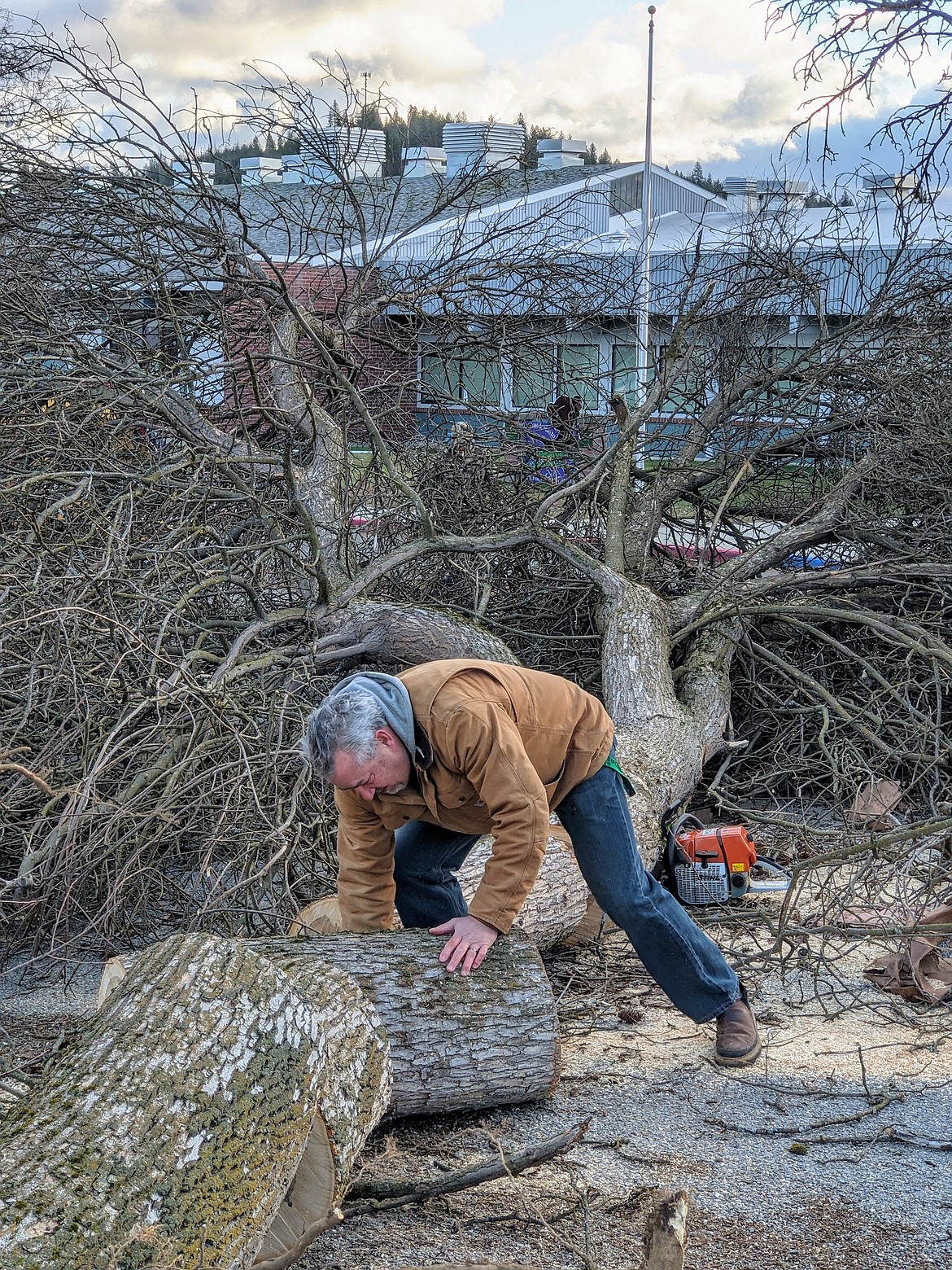 Pinehurst Elementary School Principal Mike Groves cuts up and moves a fallen tree in front of the school.