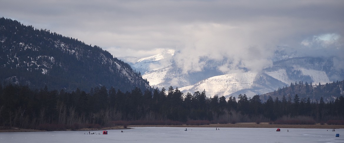 Ice fishing huts and anglers dot the surface of Dog Lake Saturday morning just off Montana 28 with the Cabinet Mountains in the background. (Scott Shindledecker/Valley Press)