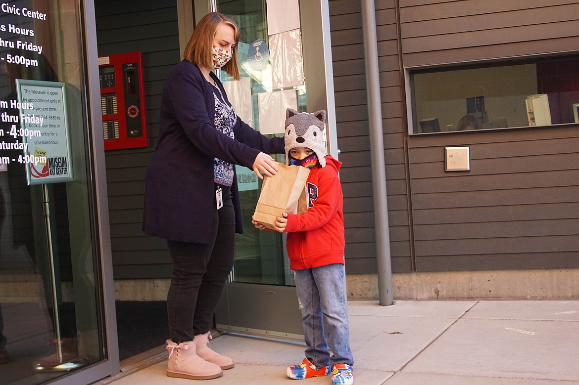 Customer service attendant Angela Hunt hands Moses Lake resident Liam Segura Jones an arts and crafts bag for Free Family Saturday.