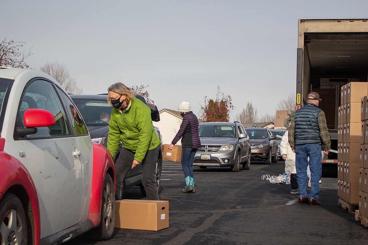 Volunteer Ruth Norman, front left, loads a box into the trunk of a car at the food box giveaway at Moses Lake Christian Church on Thursday afternoon.