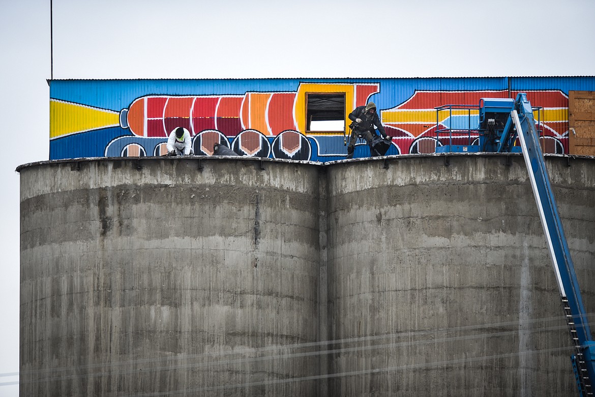 Two workers with Olympus Technical Services, of Helena, begin to remove material atop the former CHS grain elevators along West Center Street in Kalispell on Friday, Jan. 15. The site, now owned by the Flathead County Economic Development Authority, is being completely cleared except for the six grain elevators to spur development along the future Kalispell Parkline Trail. The structure atop the grain elevators, which was recently painted by local artist Thomas Valencia, is also being removed. (Casey Kreider/Daily Inter Lake)