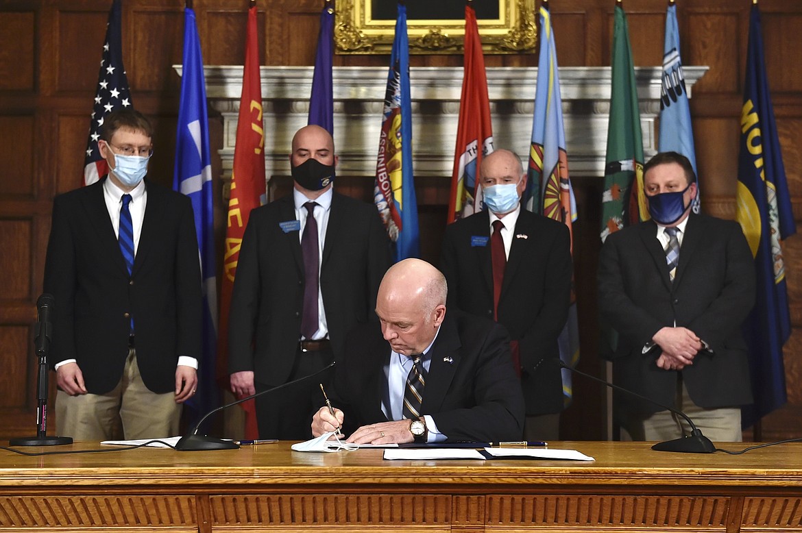 Republican Gov. Greg Gianforte signs a bill at the Montana State Capitol in Helena, Mont., Wednesday, Feb. 10, 2021, to shield businesses, health care providers, nonprofit organizations and places of worship from coronavirus-related lawsuits, provided they take measures to protect individuals from COVID-19. Gianforte also announced he would be issuing a directive on Friday to allow the state's mask mandate to expire. (Thom Bridge/Independent Record via AP)