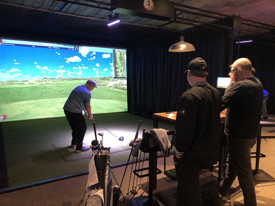 Jon Spence gets set for his shot at the simulator screen while Divots Indoor Golf owners, left to right, Henderson Orchard and Monty Buell watch from the table behind him at the business' location in Walla Walla.