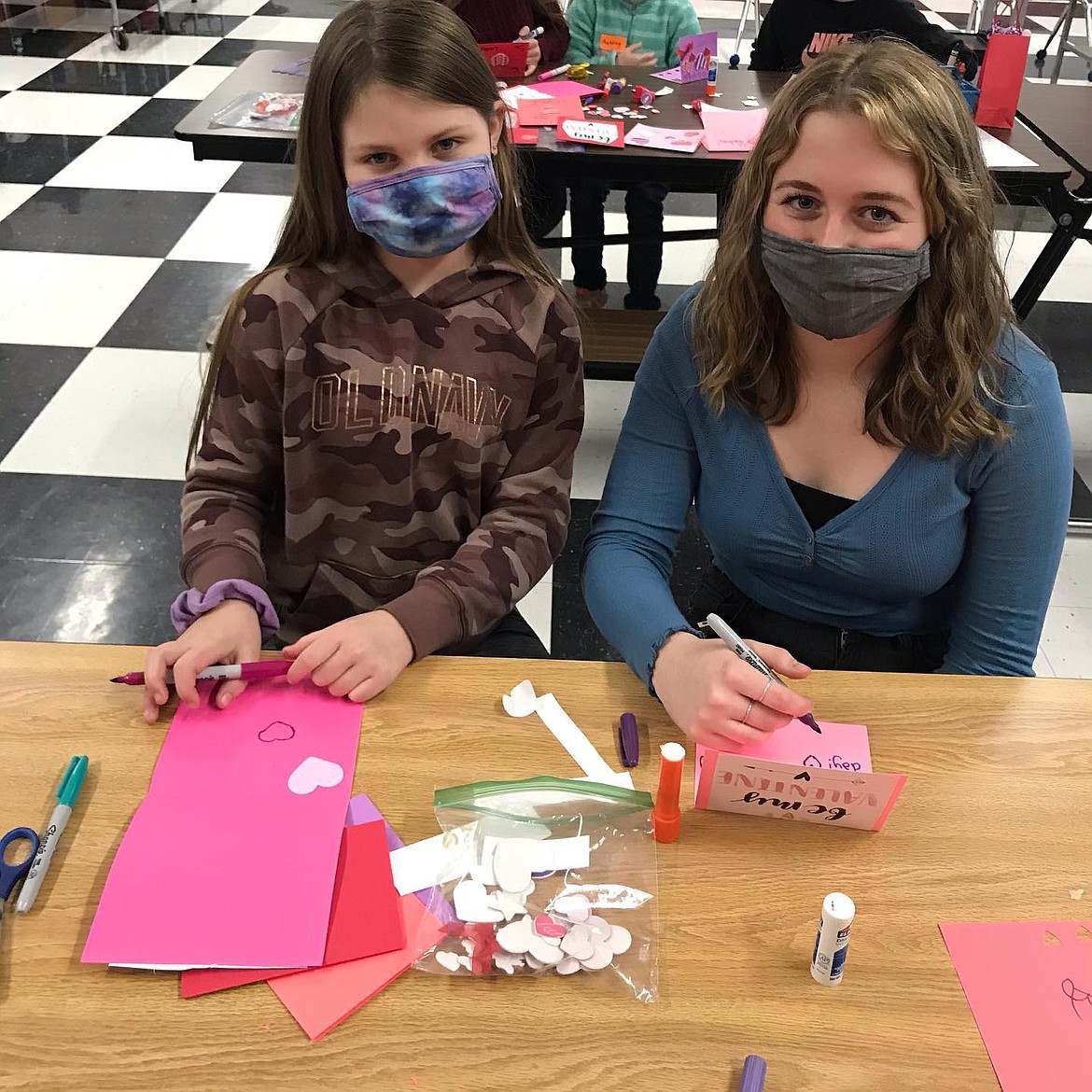 Adriana Foxx and a Little Miss smile for the camera behind their masks as they make Valentines.