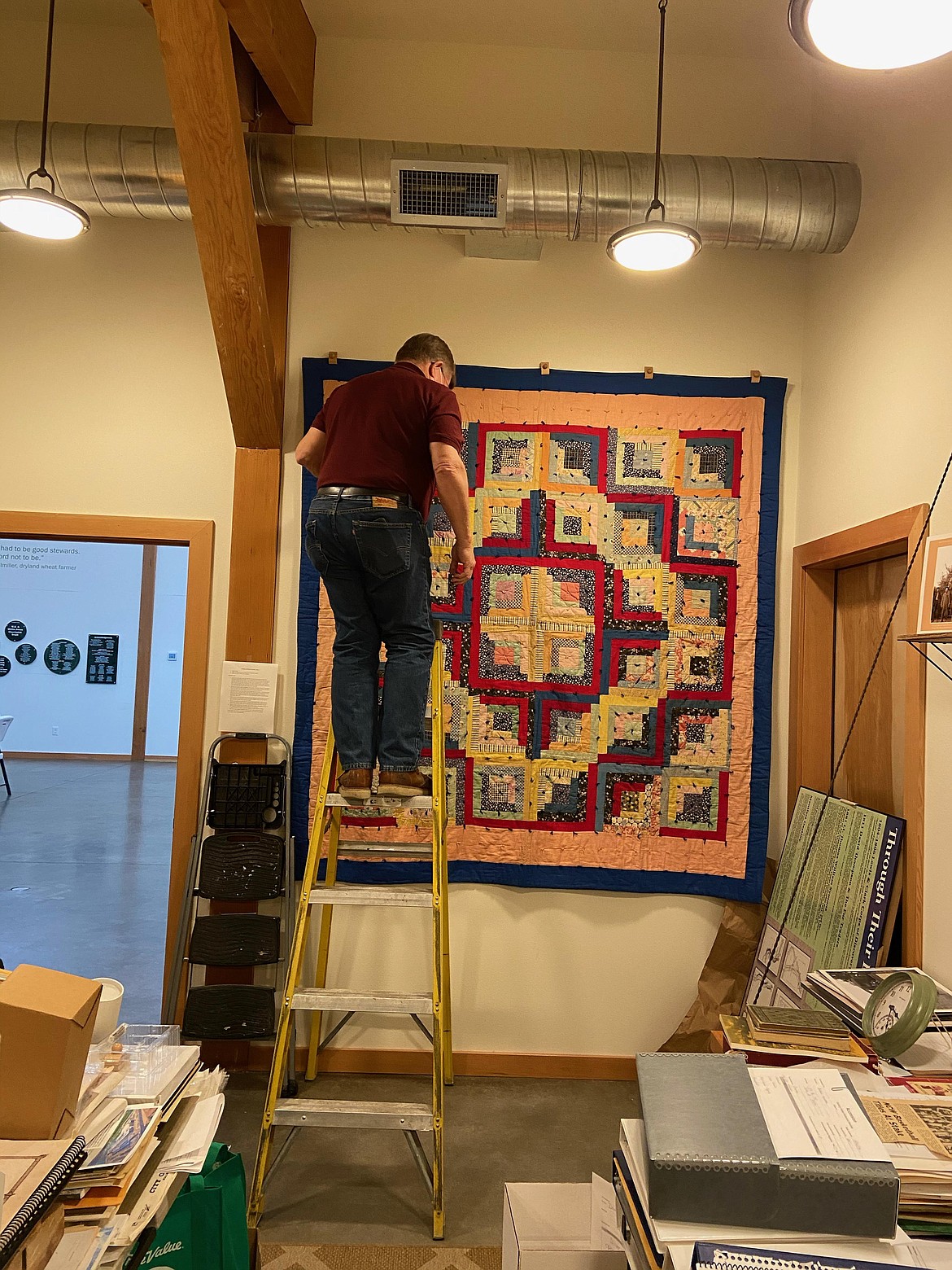 Quincy Historical Society's "skilled woodcrafter volunteer" Chris Allen hangs quilt in preparation for museum opening.