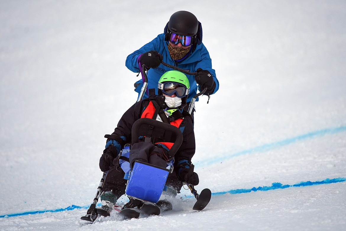 Jeffrey Sagen, with the Whitefish Schools team, crosses the finish line on a sit ski on the Alpine Novice Giant Slalom course with DREAM Adaptive instructor Bob Zahller at the Special Olympics Montana Winter Games at Whitefish Mountain Resort on Tuesday. (Casey Kreider/Daily Inter Lake)