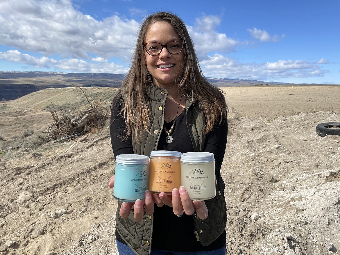 Katie Karstetter, owner of Columbia Naturals, a Quincy-based maker of lotions with CBD, holds jars of her products while standing on family farmland overlooking the Columbia River.