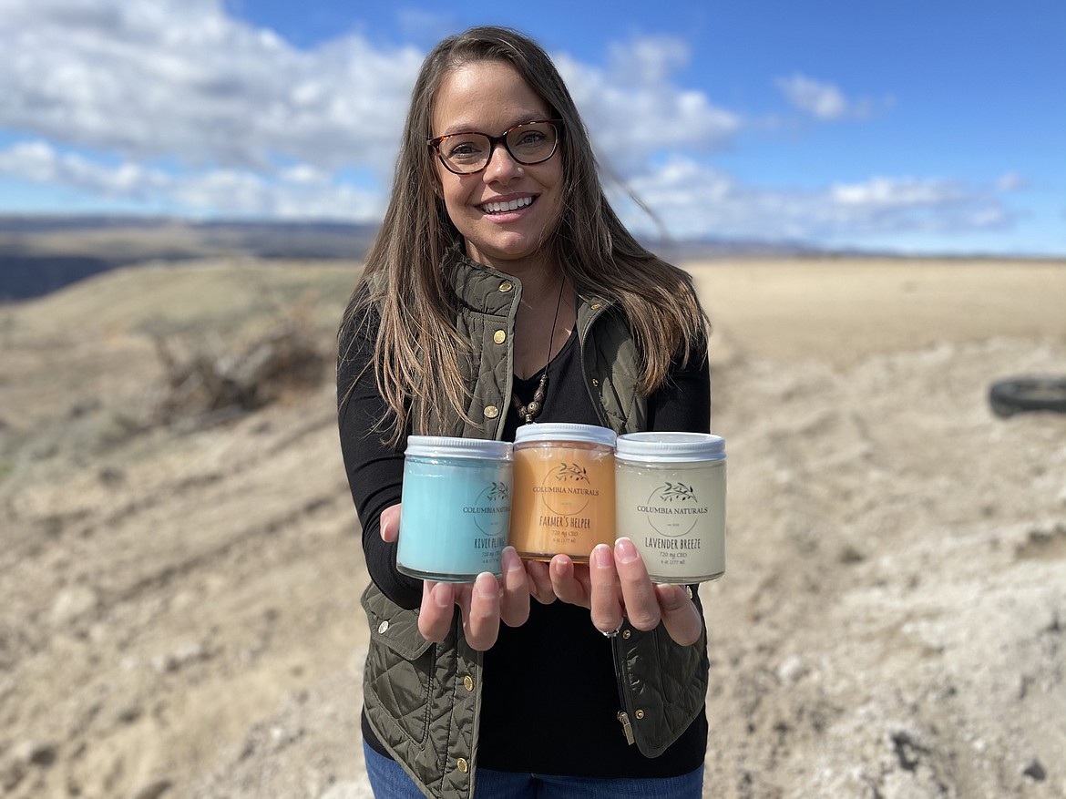 Katie Karstetter, owner of Columbia Naturals, a Quincy-based maker of lotions with CBD, holds jars of her products while standing on family farmland overlooking the Columbia River.
